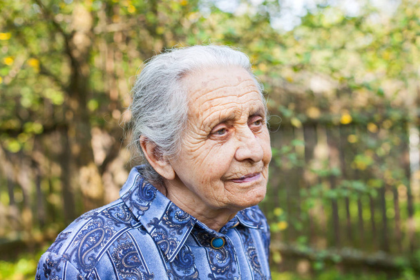 Portrait of old wrinkled lady wearing blue dress, walking in the garden on summertime - Фото, зображення