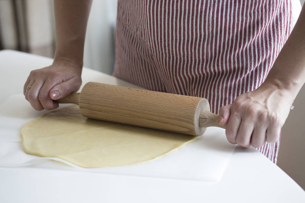 Les mains des femmes roulent la pâte sur la table de cuisine. Mains de femmes avec rouleau à pâtisserie
 - Photo, image