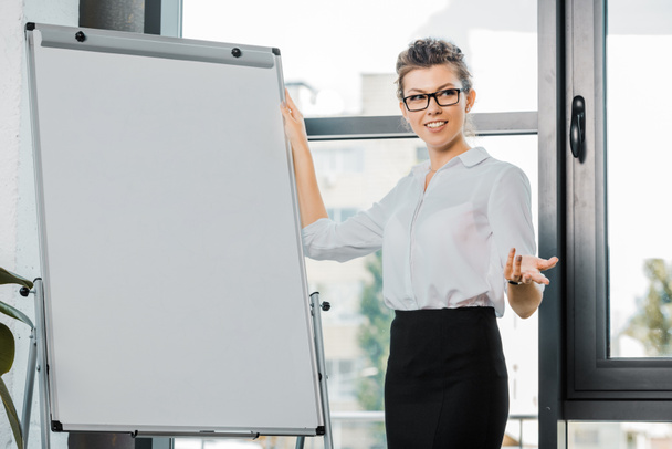 portrait of smiling businesswoman in eyeglasses standing at white board in office - Foto, imagen