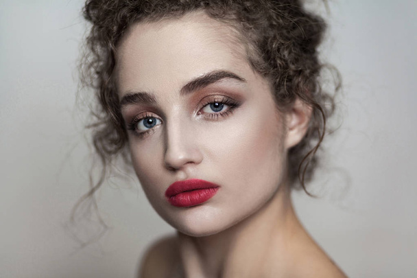 Beauty portrait of young beautiful fashion model with collected dark curly hair and nude makeup with red lips looking at camera with serious face on gray background  - Fotoğraf, Görsel