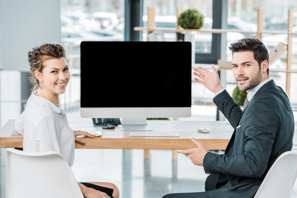 young smiling business colleagues at workplace with blank computer screen in office - Photo, Image