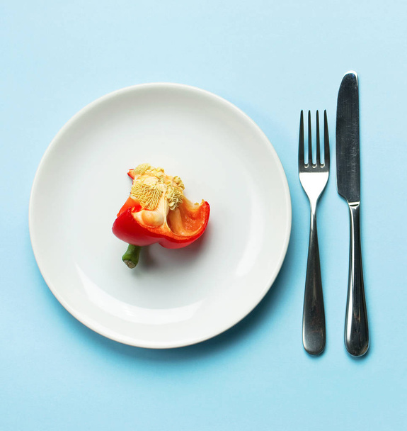 Červená paprika na bílé plotně, vidličku a nůž, diety, zdravé jídlo koncept. Čerstvý pepř, zdraví. Jídlo kreativní koncept. Pohled shora modré pozadí ploché rozložení i s kopii prostoru minimalistického stylu - Fotografie, Obrázek