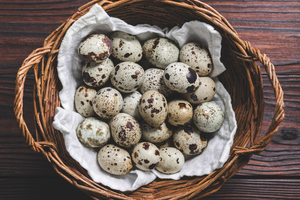 top view of raw healthy quail eggs in wicker basket on wooden table - Foto, afbeelding