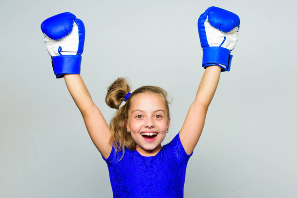 Strong child proud winner boxing competition. Girl child happy winner with boxing gloves posing on grey background. She feels as winner. Upbringing for leadership and winner. Feminist movement - Foto, afbeelding