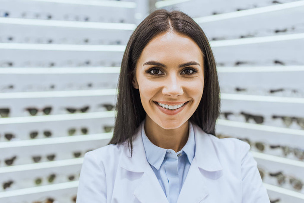 Professioneller lächelnder Augenarzt im weißen Mantel blickt in die Kamera - Foto, Bild