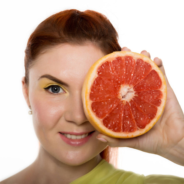 Young redhead woman with grapefruit in her hands studio portrait on a white background. concept of healthy eating - Фото, изображение