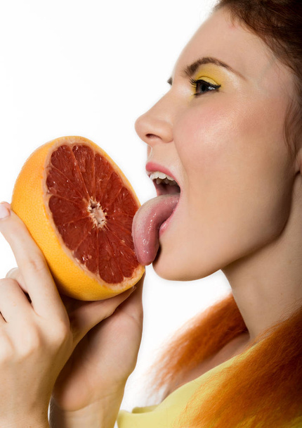 Young redhead woman licks a grapefruit on a white background. concept of healthy eating - Valokuva, kuva