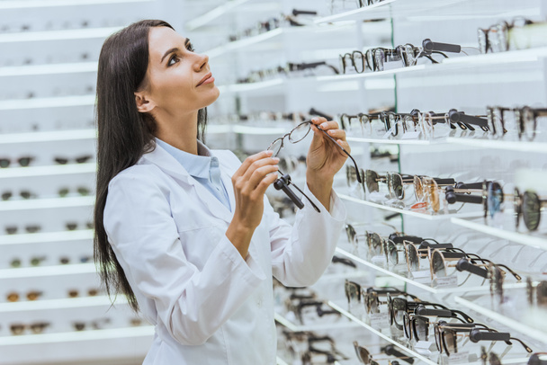 beautiful professional doctor taking eyeglasses from shelves in optica - Fotó, kép