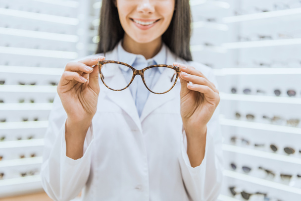 cropped view of smiling professional optometrist holding glasses - Zdjęcie, obraz