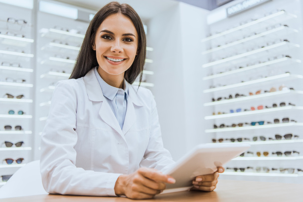 kaunis hymyilevä silmälääkäri digitaalisen tabletin avulla silmäkaupassa
 - Valokuva, kuva