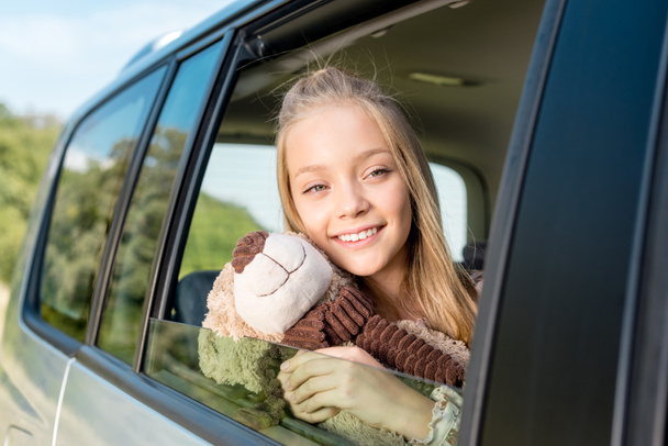 close-up portrait of smiling little child riding car on nature with teddy bear - Φωτογραφία, εικόνα