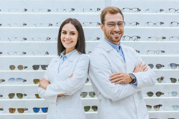 professional opticians posing with crossed arms in ophthalmic shop with glasses - Photo, Image