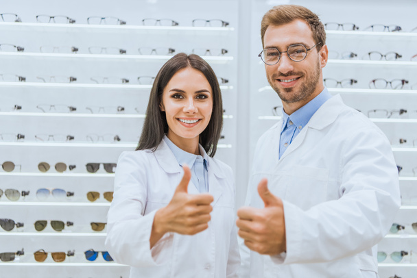 zawodowe lekarzy w białych płaszczach pokazano kciuki w optyce ze wzrokiem na półkach - Zdjęcie, obraz