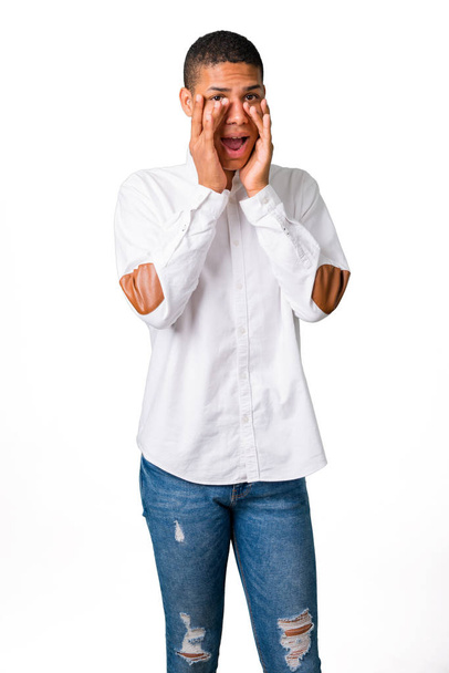 Young african american man with white shirt surprised and covering face with hands while looking through fingers on isolated white background - Photo, image