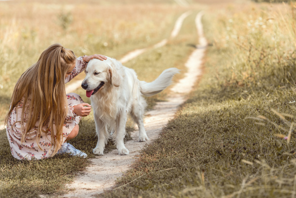 beautiful little child with adorable golden retriever dog in field - Valokuva, kuva