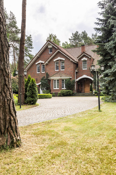 großes Einfamilienhaus außen mit Ziegelwänden und rotem Dach hinter einem Kopfsteinpflasterweg und im Sommer grünem Rasen - Foto, Bild
