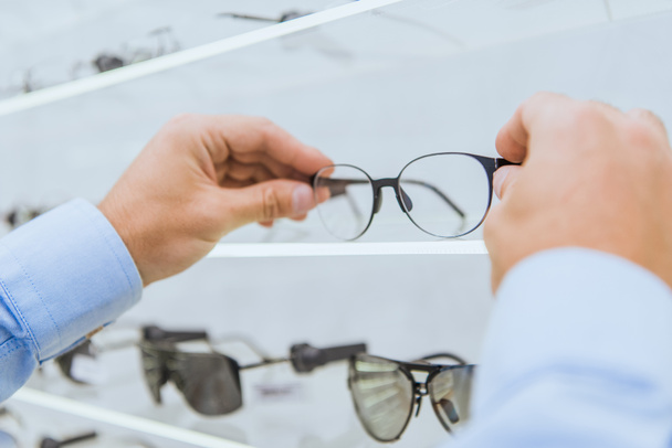 cropped view of person taking eyeglasses from shelf in optica - Fotografie, Obrázek