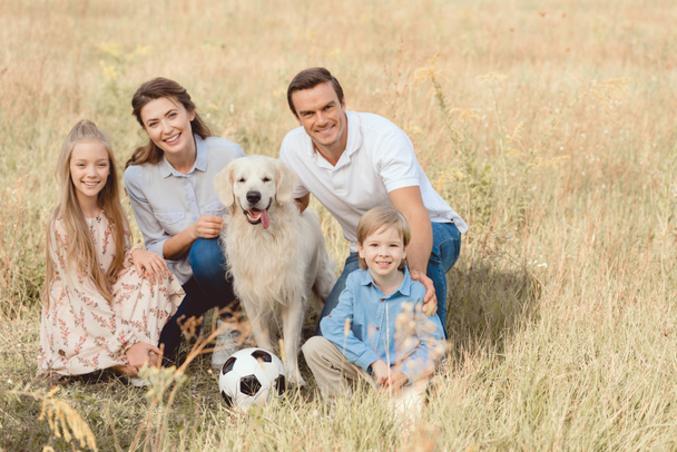 happy young family with retriever dog sitting in field together and looking at camera - Foto, Bild