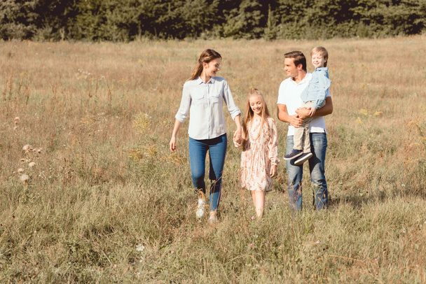 onnellinen nuori perhe kävelee pellolla yhdessä
 - Valokuva, kuva