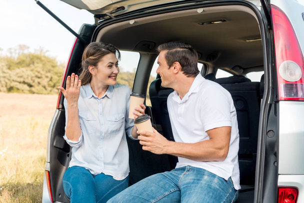 felice coppia adulta con tazze di carta di caffè seduto nel bagagliaio dell'auto durante il viaggio in auto
 - Foto, immagini