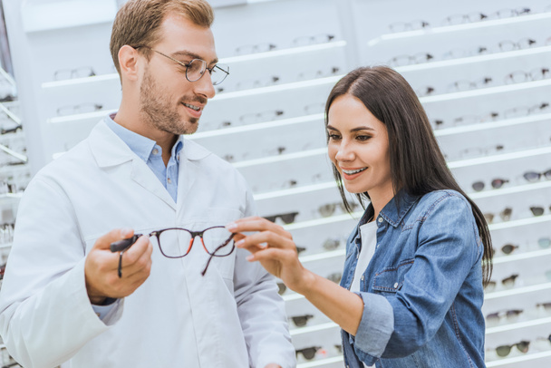 Selektivní fokus mužské optik ukazující brýle na usmívající se žena v optica - Fotografie, Obrázek