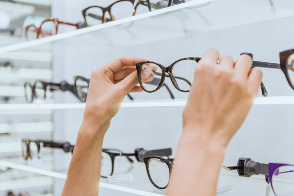 partial view of optician taking glasses from shelf in ophthalmic shop - Photo, Image