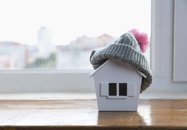 house in winter - heating system concept and cold snowy weather with model of a house wearing a knitted cap - Foto, Imagen