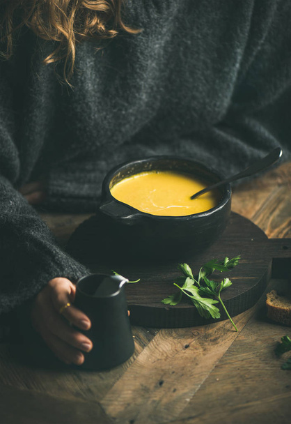 Woman in dark grey winter sweater eating sweet corn and shrimp chowder soup from black bowl. - Foto, immagini