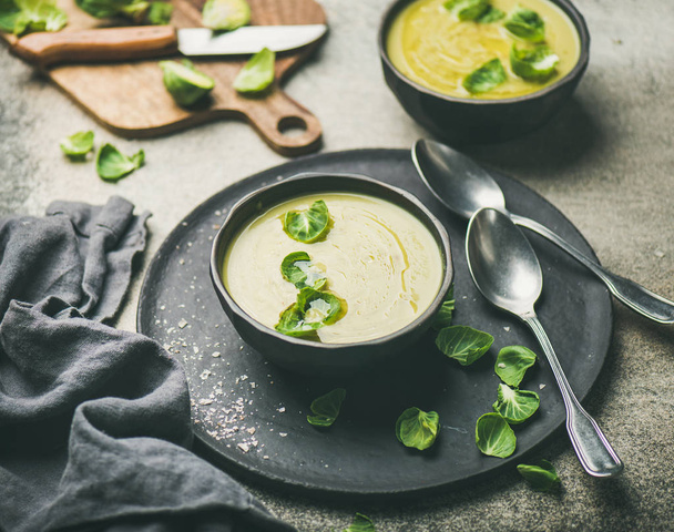 Seasonal brussels sprouts vegetable cream soup in black bowl and fresh green brussel sprouts over grey concrete background - Fotoğraf, Görsel