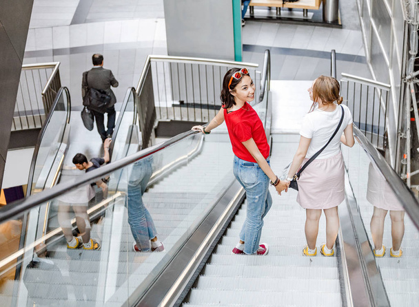 feliz jovem mulher amigos na escada rolante no shopping
 - Foto, Imagem