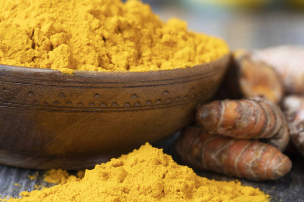 Turmeric powder in a wooden bowl and on the table with turmeric roots. - Foto, Imagen