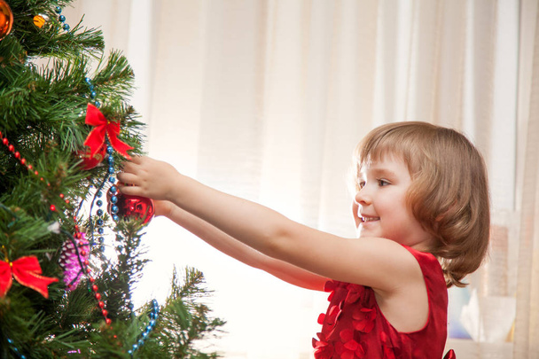 Little girl decorating christmas tree with toys and baubles. Cute kid preparing home for xmas celebration. - Photo, Image