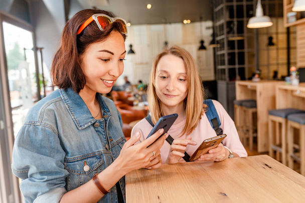 Két fiatal nő ül a kávézó, és használ smartphone, wi-fi internet kapcsolat fogalma - Fotó, kép