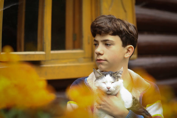 teenager boy cuddle with cat close up photo on summer cottage house country background - Photo, Image