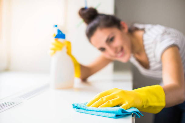 Close-up the young smiling woman in yellow gloves washing windowsill with rag and window cleaner indoors - 写真・画像