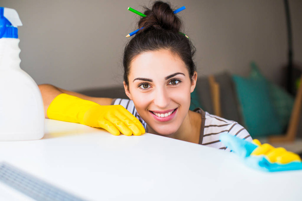 Portrait of the young smiling woman in yellow gloves who holding rag and washing windowsill in the room - Foto, Imagem