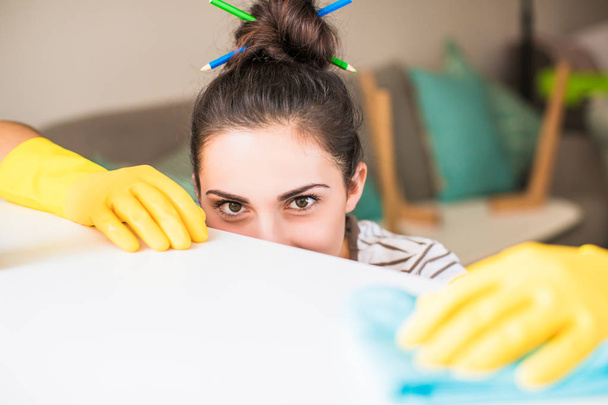 Close-up the young smiling woman in yellow gloves holding rag and washing windowsill in the room - 写真・画像