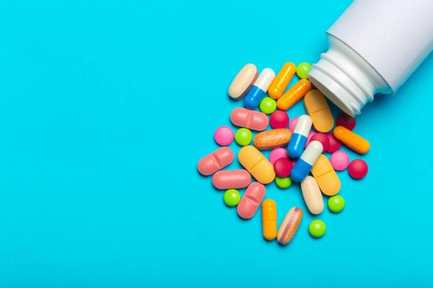 colorful pills scattered from bottle over blue background - Foto, immagini