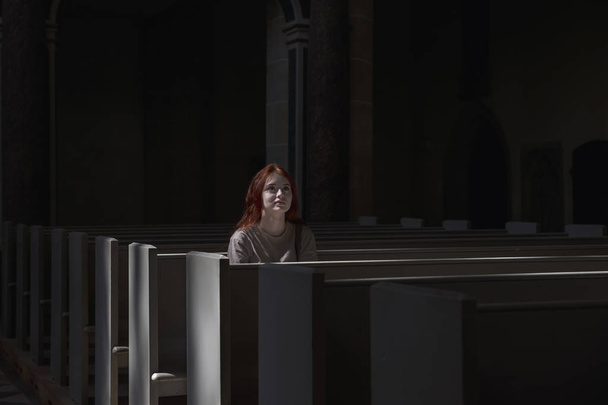 Jovem menina ruiva bonita solitária senta-se na igreja orando a Deus com fé olhando para a frente
 - Foto, Imagem