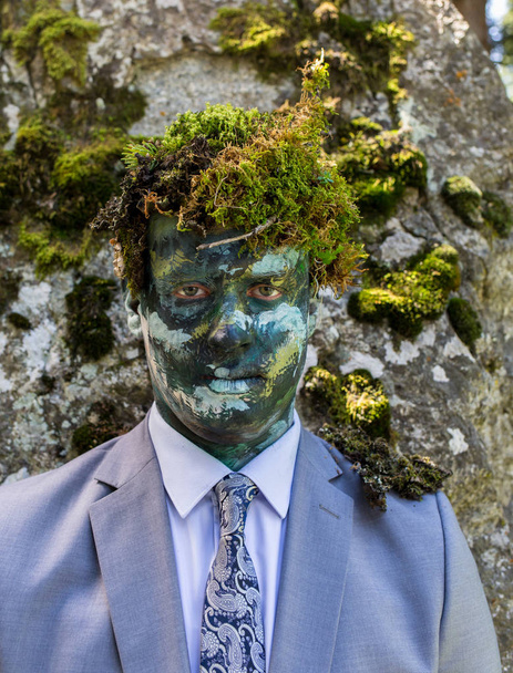 Trabajador de oficina con traje de trabajo, al aire libre con maquillaje en la cara y musgo verde en la cabeza. El hombre se funde con la naturaleza
. - Foto, imagen