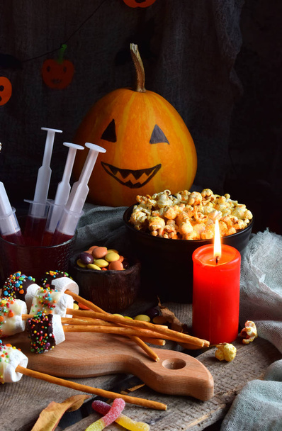 Halloween trick or treat party. Funny delicious sweets and pumpkin on wooden background - muffins, cupcakes, marshmallows, popcorn, juice, jellies, candy - Zdjęcie, obraz
