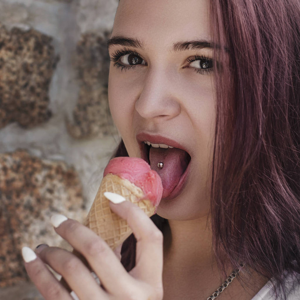 Young red-haired girl juicy licking ice cream with red tongue with piercings - Photo, Image