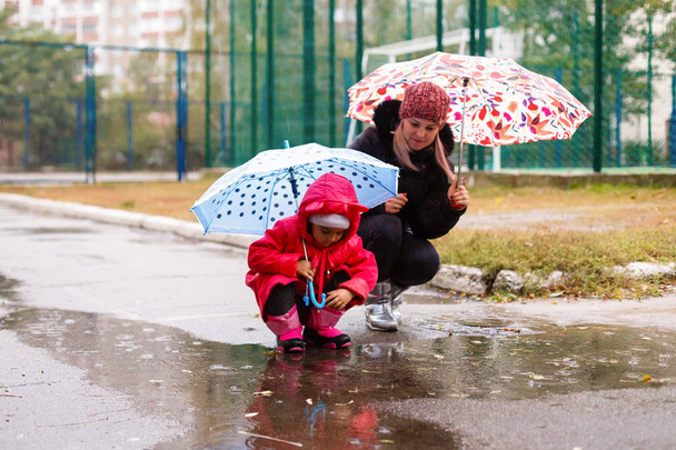 Joven hermosa mujer con hija bonita caminando en el parque con paraguas
 - Foto, Imagen