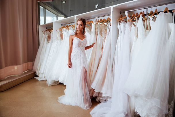 Beautiful bride is trying on an elegant wedding dress in modern wedding salon - Фото, изображение