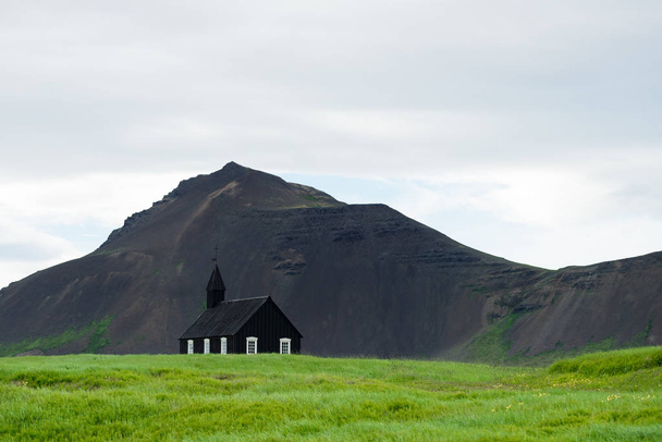 Чёрная церковь в деревне Будир, Исландия. Религиозные и туристические достопримечательности. Летний пейзаж с часовней и горной вершиной
 - Фото, изображение