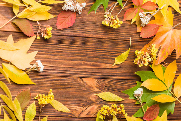 Banner de otoño con hojas coloridas de árboles y flores secas sobre fondo marrón de madera - marco de otoño natural con follaje y espacio de copia para el saludo de temporada o cartel de promoción
. - Foto, Imagen