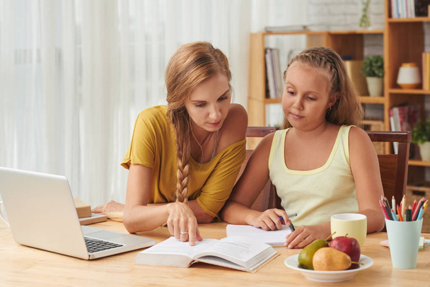 біла мати і дочка виконують домашнє завдання за столом з книгою
  - Фото, зображення