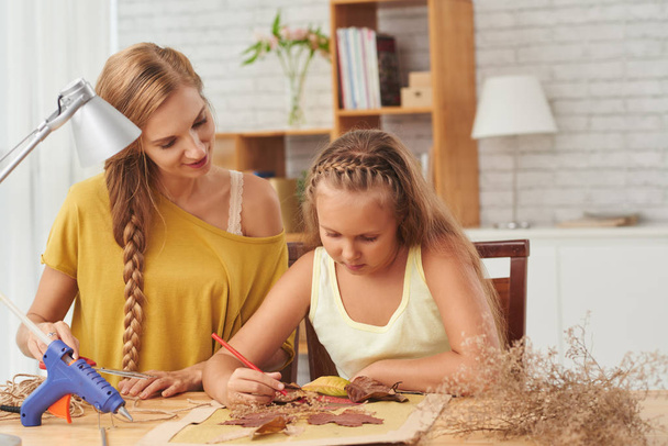 caucasian mother and daughter creating handmade decoration picture with dry leaves and flowers  - Photo, image