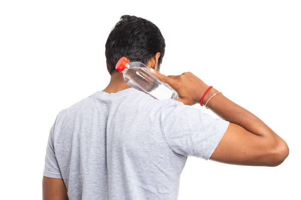 Persona indiana che tocca la parte posteriore del collo con una bottiglia d'acqua di plastica non guardando la fotocamera isolata sul bianco come rimanere concetto idratato
 - Foto, immagini