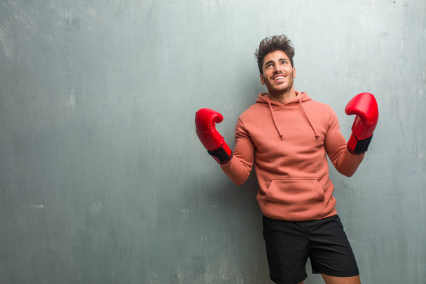 Jonge fitness man met bokshandschoenen tegen een muur van de grunge lachen en plezier - Foto, afbeelding